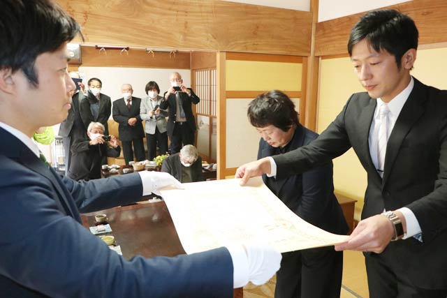 滝沢市長(左)から佐藤宗司さんへの勲章や位階の伝達を受ける二男智広さん、妻アキさん