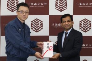 ゴッドハンドの角田代表取締役(左)から三条市立大学のシャハリアル学長に1,128万円の目録を手渡す