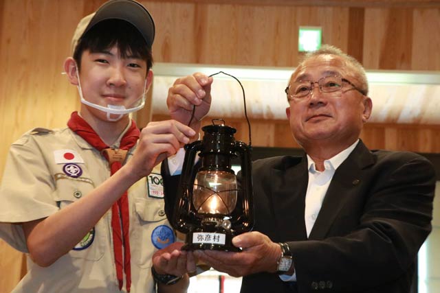 起こした火をランタンに移して小林豊彦弥彦村長(右)に手渡すボーイスカウト西蒲原第七団ボーイ隊の赤坂さん(左)