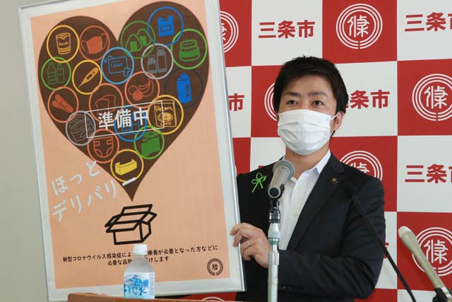 「ほっとデリバリー」のポスターを手に臨時記者会見を行う滝沢三条市長