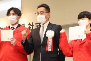 コメリグループ入社式で捧社長が新入社員のユニホーム着用を手伝って仲間に
