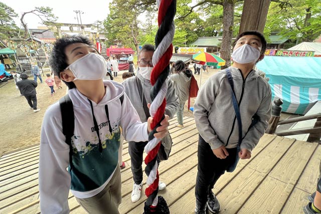 新しい鈴緒を引きぴかぴかの鈴を鳴らす参拝者