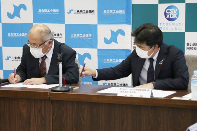 協定書に署名する兼古会頭と水越支店長