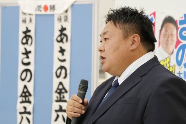 おじの浅野金六氏のたすきを掲げて選挙事務所で事務所開きのあいさつをする佐野氏