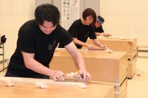 桐かんなかけ大会に挑戦する左から地域おこし協力隊の松本さん、藤田加茂市長、加茂桐箪笥伝統工芸士会会長の三本さん