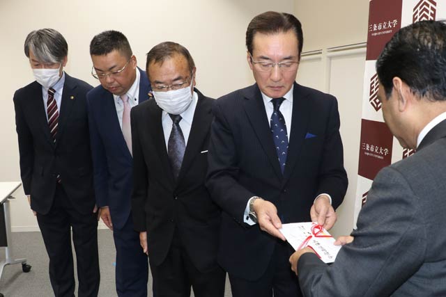三条信用組合の佐藤理事長から三条市立大学のシャハリアル学長に目録を手渡す