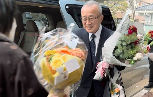 玄関前で支持者から花束を受け取る小林村長