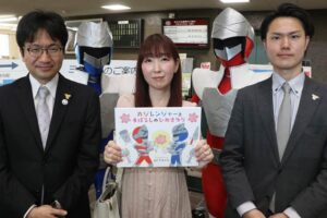 絵本『カジレンジャーとまぼろしのひめさゆり』と左から三条商工会議所青年部の山村会長、絵と文のあだちさん、DX広報委員会の佐藤委員長、後ろに燕三条戦隊スーパーカジレンジャー
