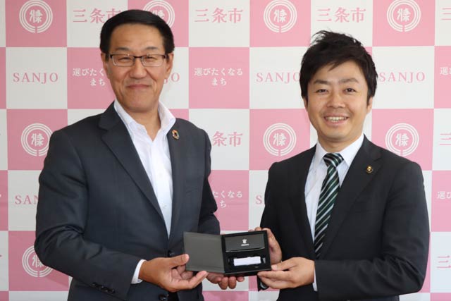 三条信用金庫の白倉理事長(左)から軟骨伝導イヤホンを受け取る滝沢市長