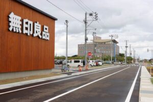 ショッピングセンターわきに新設された道路と写真右奥の交差点の先、協栄信用組合本店の東側に「廿六木四」停留所を新設する