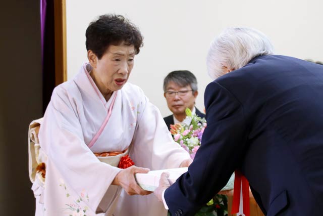 堀会長から熟年成人者への記念品を代表で受け取る佐渡山長寿クラブ会長の吉野サキさん(79)