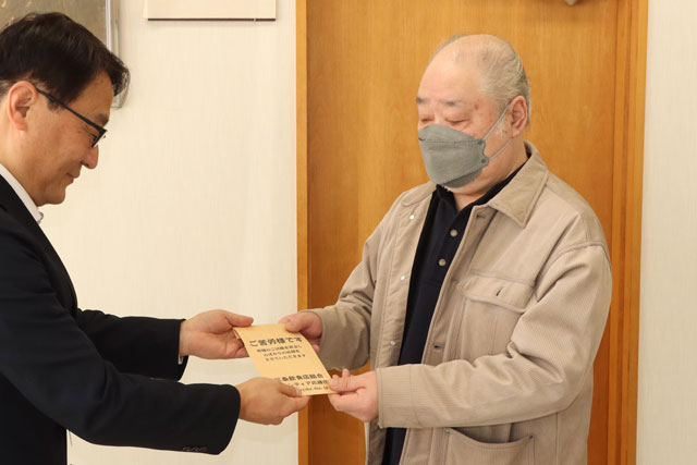 笹川市社協事務局長(左)にラーメン無料券を手渡す三条飲食店組合の阿部組合長