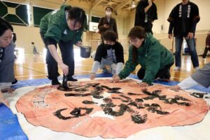 三条六角巻凧に「笑顔の輪」と筆で書く能登高校書道部員
