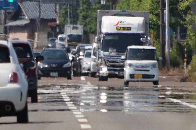 熱くなったアスファルトからの熱気で景色が揺らぎ逃げ水が（三条市上須頃地内の市道大島164号）