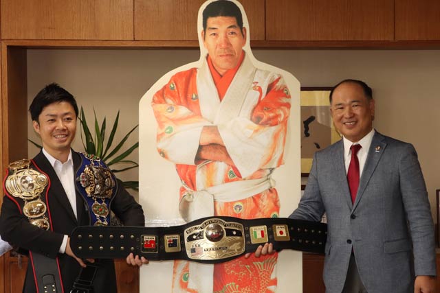 滝沢市長(左)と馬場さんが巻いたチャンピオンベルトのレプリカ3本を寄付した中條さん