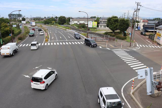 「直江(二)交差点」、写真手前から右折する軽自動車と奥から手前へ直進する普通車がぶつかった