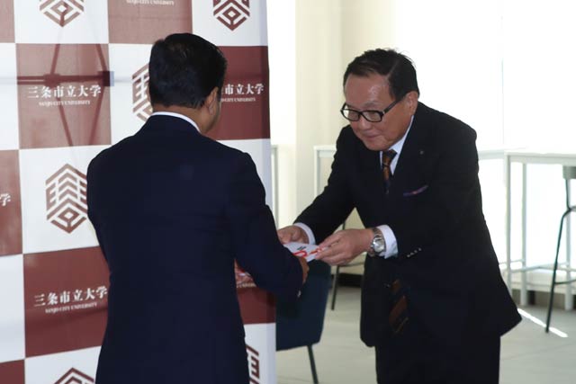 渡辺会長からシャハリアル学長に国旗掲揚塔一式の目録を手渡す