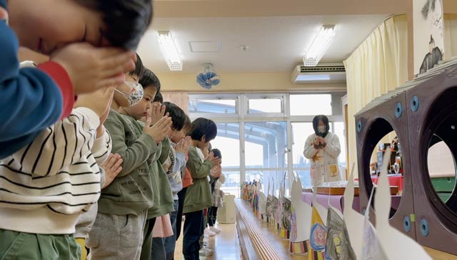菅原道真の掛け軸に手を合わせて頑張ることを祈る園児
