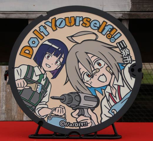 オリジナルテレビアニメ「Do It Yourself!! -どぅー・いっと・ゆあせるふ-」ご当地マンホールのふた