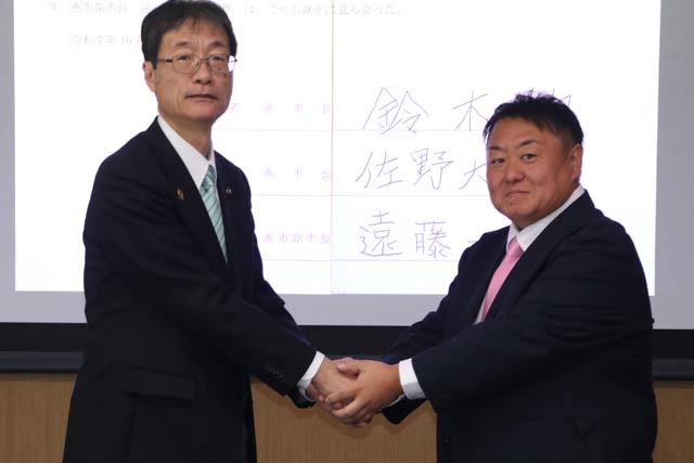 事務引継書に署名して握手する鈴木市長(左)と佐野新市長