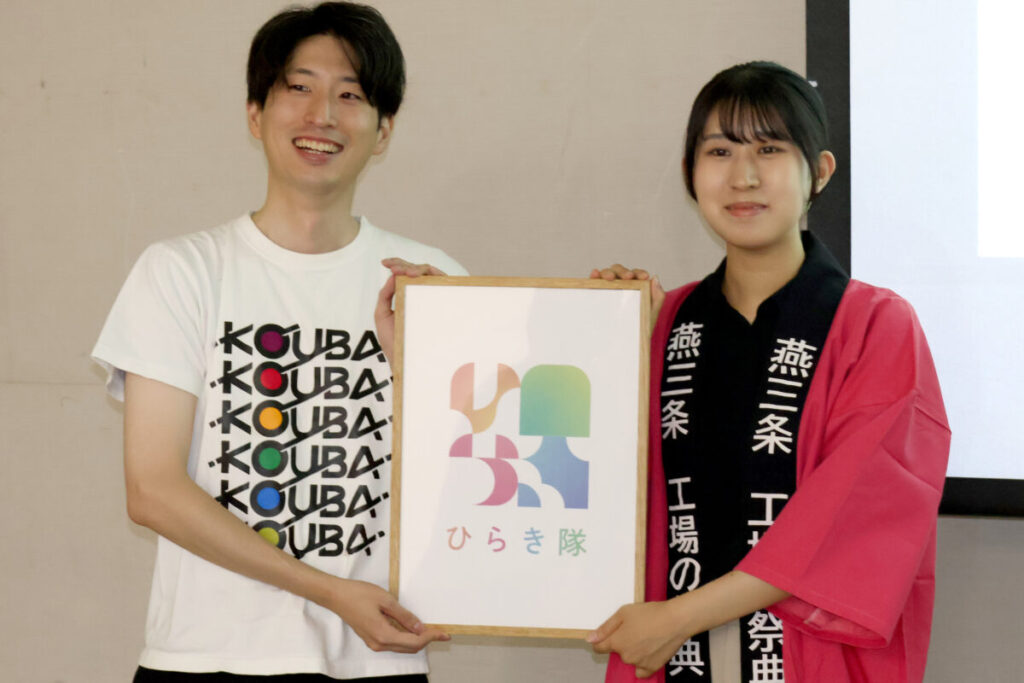 8月23日に発足したひらき隊で発表されたプリプレスの加藤さん(右)がデザインしたひらき隊のロゴ